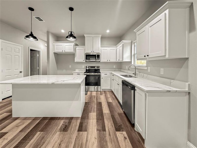 Kitchen featuring stainless steel appliances, white cabinetry, light stone counters, a kitchen island, and hanging light fixtures