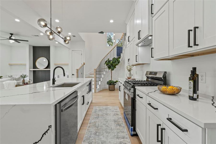 Kitchen with stainless steel appliances, white cabinetry, light stone counters, light wood-style floors, and open floor plan