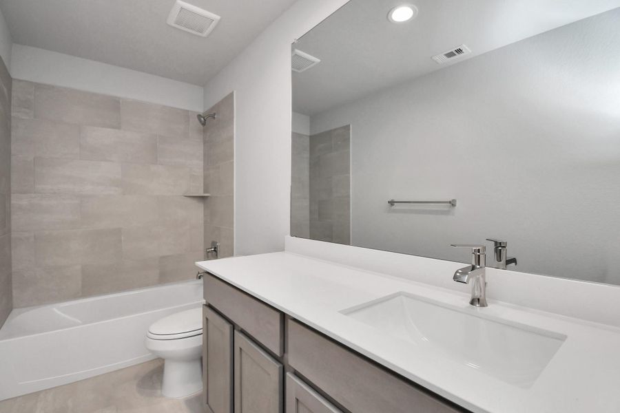 Secondary bath features tile flooring, bath/shower combo with tile surround, light stained wood cabinets, beautiful light countertop. Sample photo of completed home with similar floor plan. Actual colors and selections may vary.
