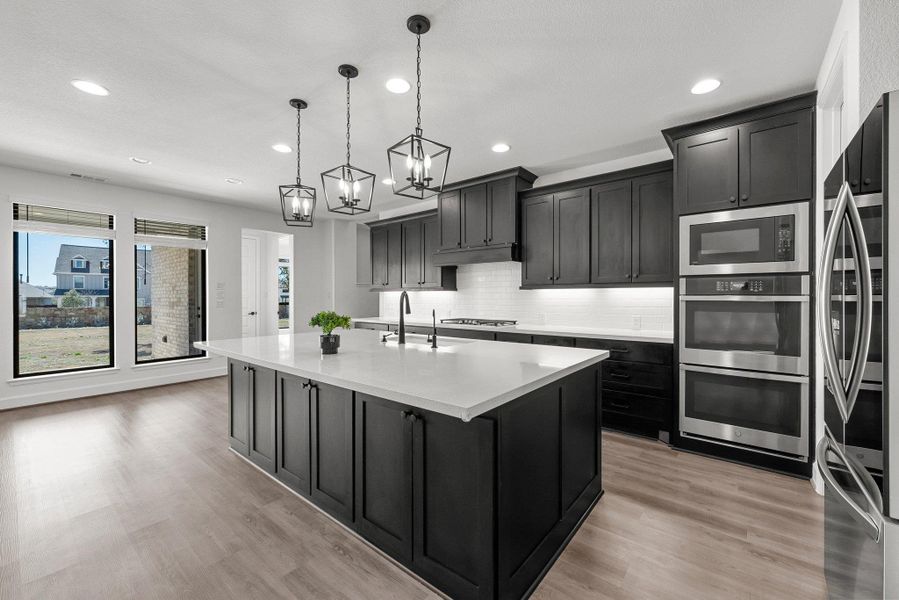 Kitchen featuring light wood finished floors, light countertops, decorative backsplash, appliances with stainless steel finishes, and a sink