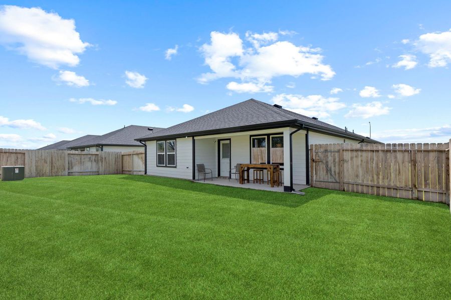 Rear exterior view shows the home’s extended covered patio and generous lawn space, ready for gatherings, playtime, or peaceful evenings outdoors. Full gutter system and sprinkler system Rear exterior view shows the home’s extended covered patio and generous lawn space, ready for gatherings, playtime, or peaceful evenings outdoors. Full gutter system and sprinkler system