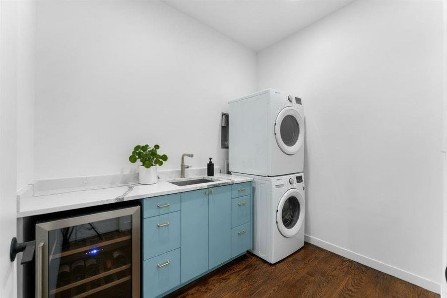 Laundry room with estacked washer and dryer, dark wood finished floors, beverage cooler, and cabinet space