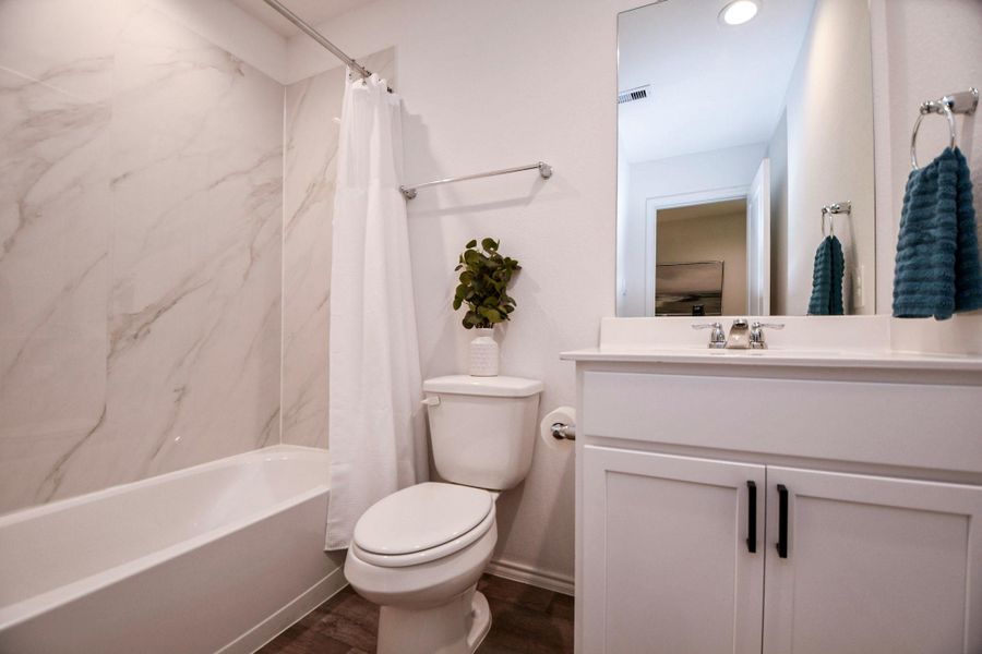 This bathroom features a modern design with a marble-look shower surround, a white vanity, and chrome fixtures.