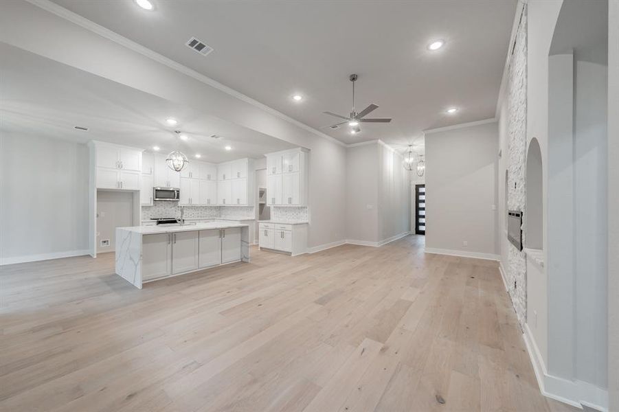 Kitchen with open floor plan, crown molding, a chandelier, light wood-style flooring, and a kitchen island with sink
