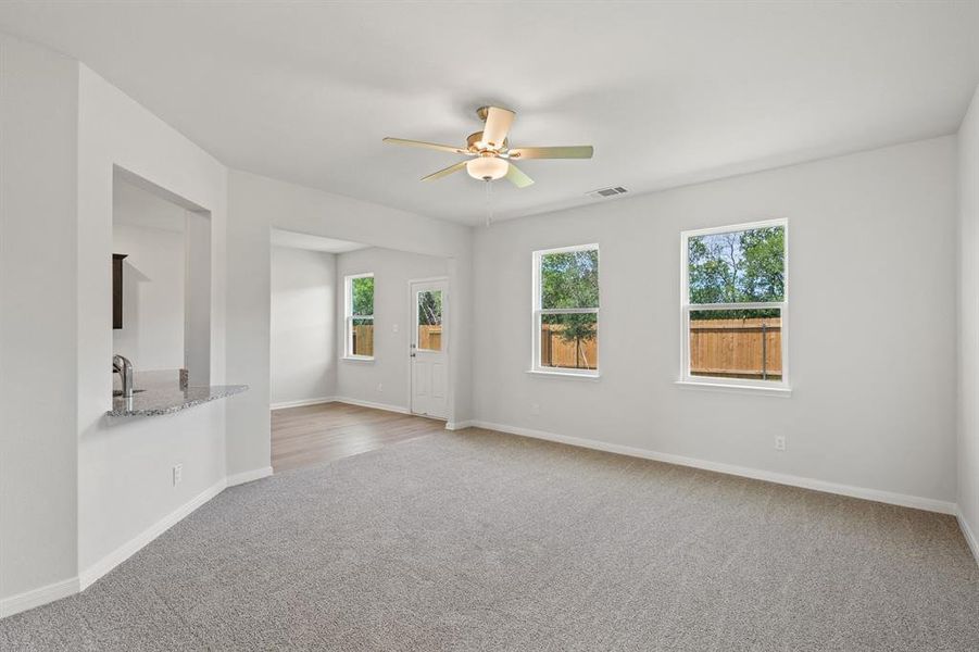 Carpeted empty room featuring a healthy amount of sunlight, baseboards, a ceiling fan, and visible vents