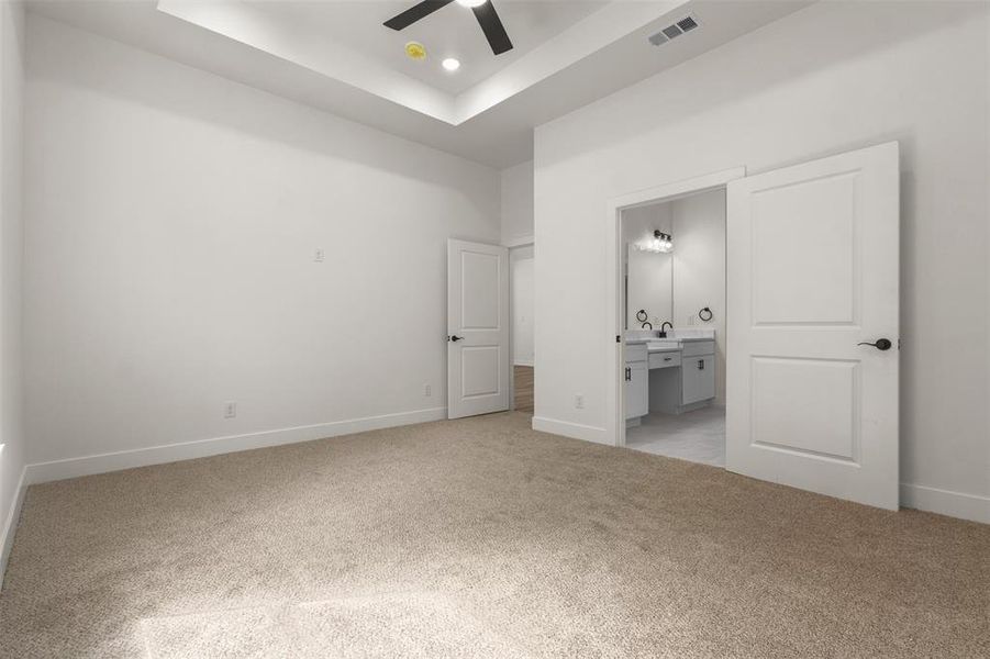 This room features light-colored carpeting, white walls, and a tray ceiling with recessed lighting