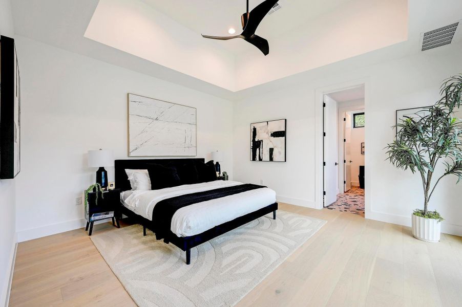 Bedroom with a tray ceiling, light wood-style flooring, and ceiling fan