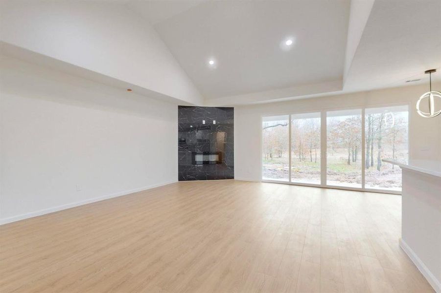Unfurnished living room featuring high vaulted ceiling, light wood-type flooring, and baseboards