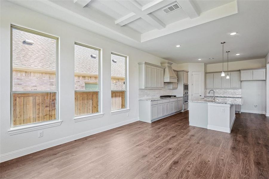 Kitchen with light stone counters, dark hardwood / wood-style floors, a kitchen island with sink, decorative backsplash, and decorative light fixtures