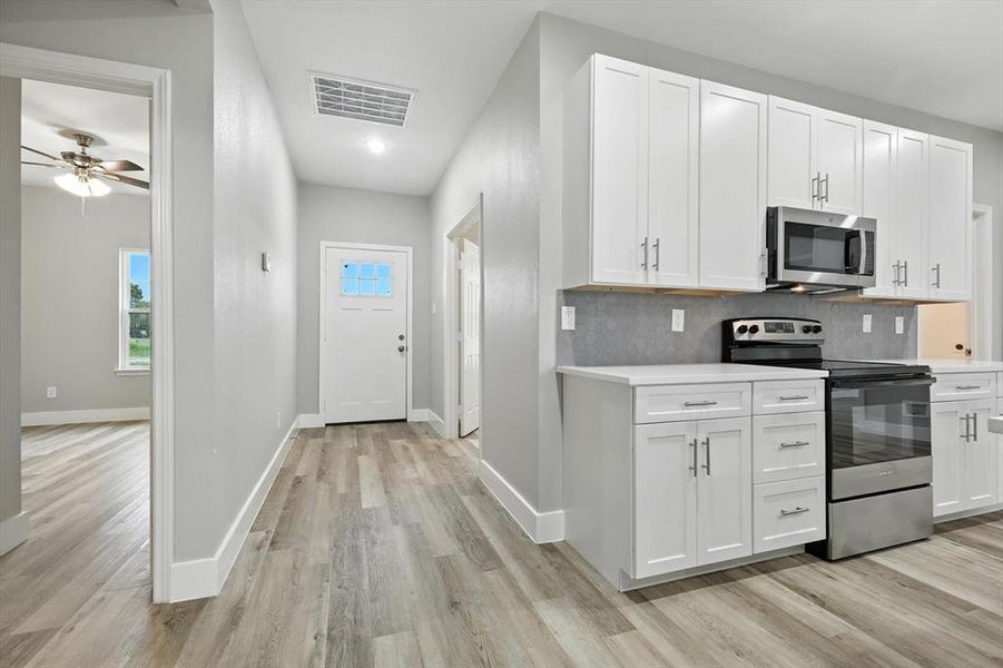 Kitchen featuring appliances with stainless steel finishes, white cabinetry, backsplash, light wood-type flooring, and ceiling fan Kitchen featuring appliances with stainless steel finishes, white cabinetry, backsplash, light wood-type flooring, and ceiling fan
