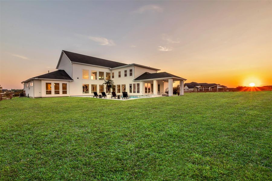 Rear Elevation:At sunset, the residence unveils its grandeur across an expansive lawn, where walls of glass reflect golden skies and indoor living flows seamlessly outdoors. This sweeping vantage captures the home’s scale, serenity, and the promise of refined gatherings beneath open Texas horizons.