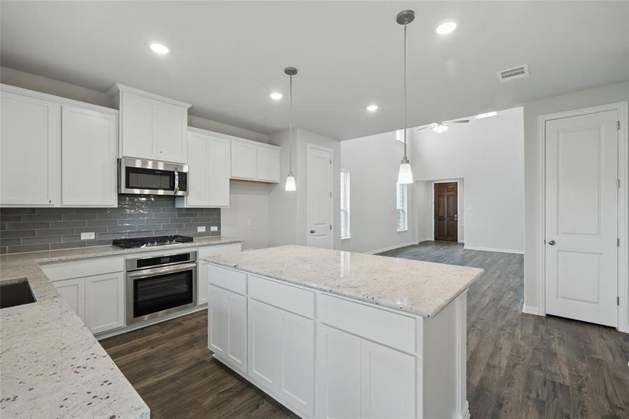 Kitchen featuring stainless steel appliances, tasteful backsplash, dark wood finished floors, white cabinetry, and light stone countertops