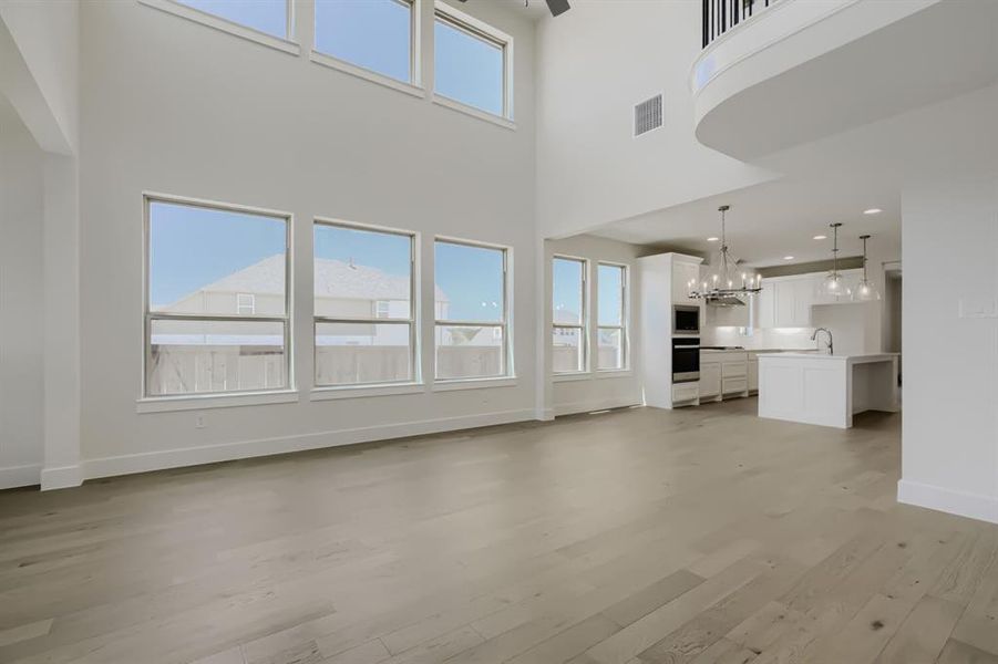 Open-concept living area featuring a two-story ceiling, light wood-finish flooring, and an abundance of natural light through multiple windows