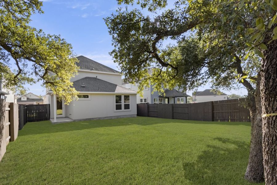 Image of back exterior of a two story home with a large green grass backyard with trees and a wooden fence Image of back exterior of a two story home with a large green grass backyard with trees and a wooden fence
