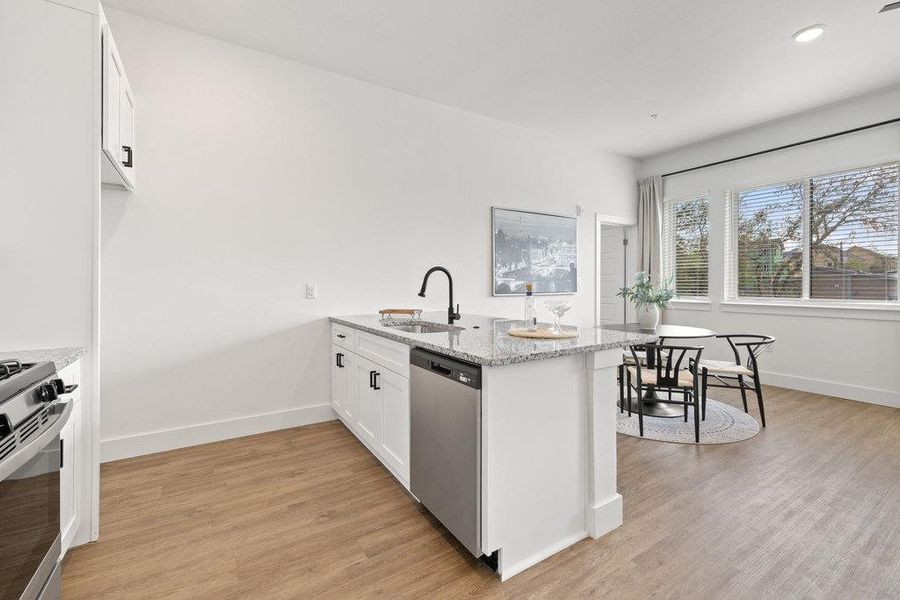 Kitchen with a peninsula, white cabinetry, light stone countertops, appliances with stainless steel finishes, and light wood-style floors
