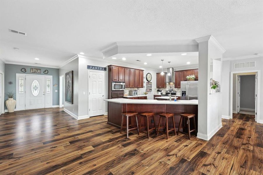 Kitchen featuring pendant lighting, wall chimney range hood, a breakfast bar, appliances with stainless steel finishes, and decorative backsplash