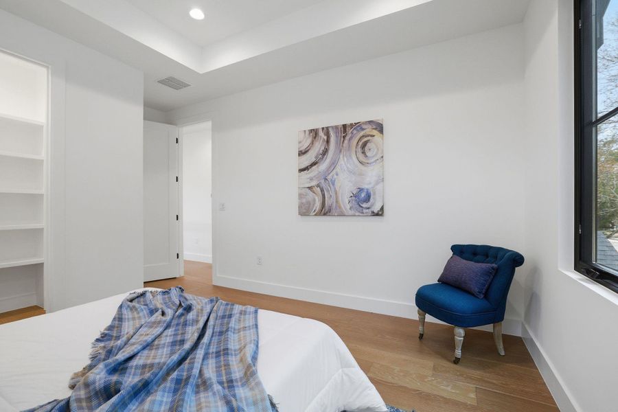Bedroom featuring a spacious closet, light wood finished floors, recessed lighting, and a raised ceiling