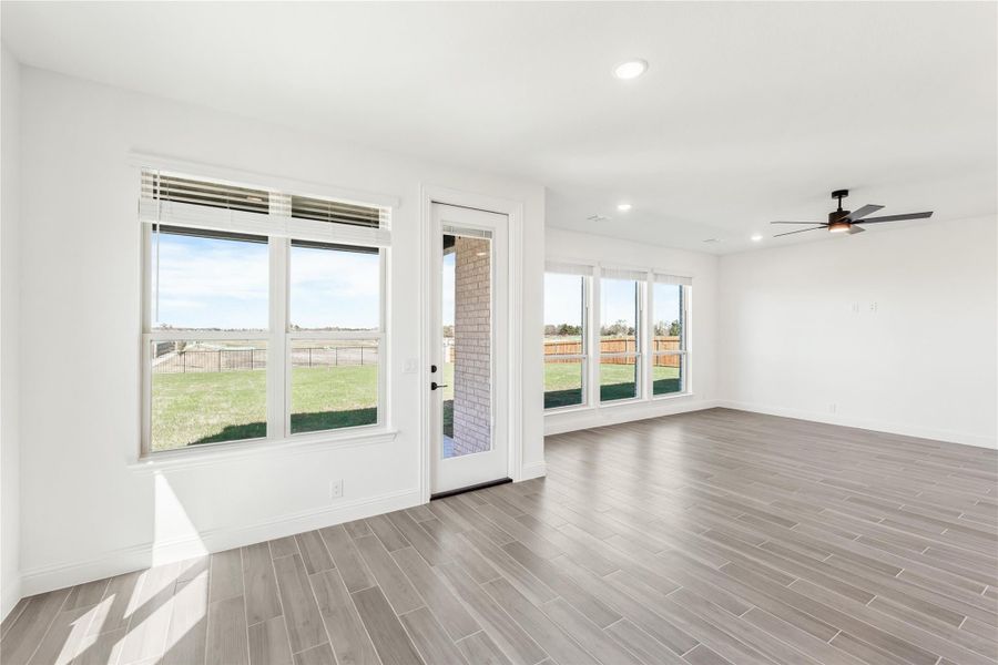 Open living area with wood-look tile floors, ceiling fan, and large windows overlooking a fenced backyard Open living area with wood-look tile floors, ceiling fan, and large windows overlooking a fenced backyard