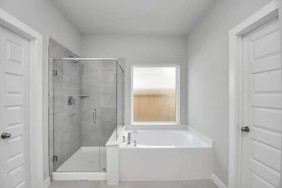 Escape to a spa-like oasis in this primary bathroom. Enjoy a walk-in shower with tile surround, a separate garden tub with custom detailing, and an elegant vanity featuring light countertops, modern hardware, and beautiful recessed lights. Experience luxury and relaxation in every detail. Sample photo of completed home with similar floor plan. Actual colors and selections may vary.