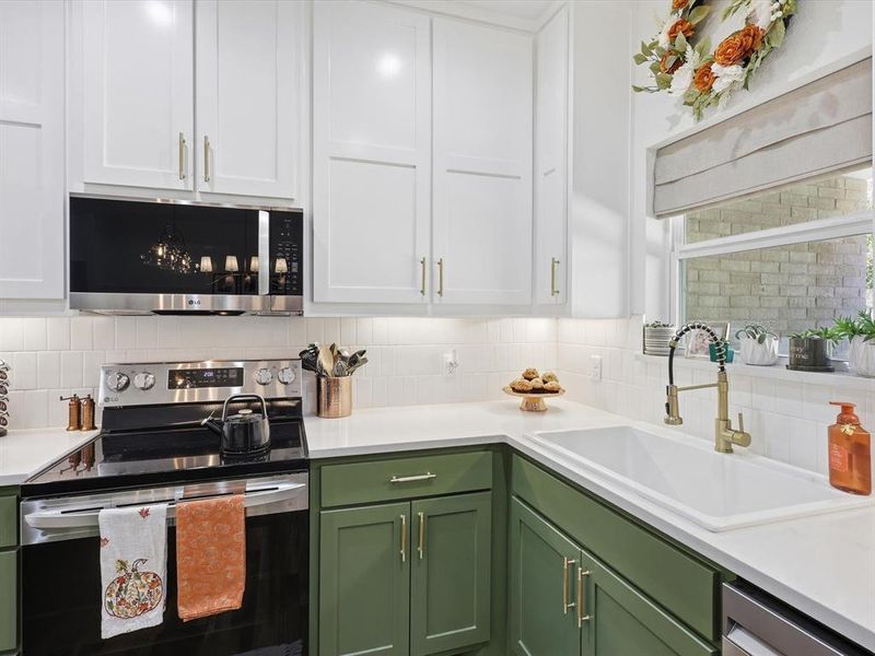 Kitchen featuring green cabinetry, appliances with stainless steel finishes, white cabinetry, and tasteful backsplash