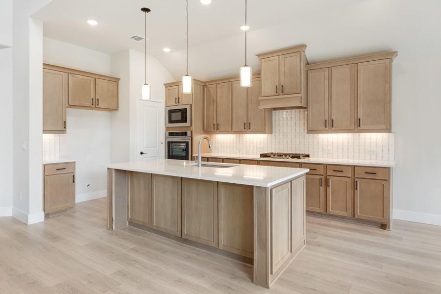 Kitchen with light wood cabinets, large island with white countertop, pendant lights, and stainless steel appliances