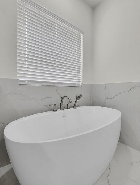 Bathroom featuring tile walls, a soaking tub, marble finish floors, and wainscoting