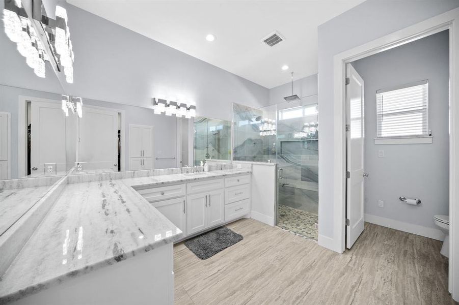 Bathroom featuring a marble finish shower, vanity, light wood finished floors, and recessed lighting