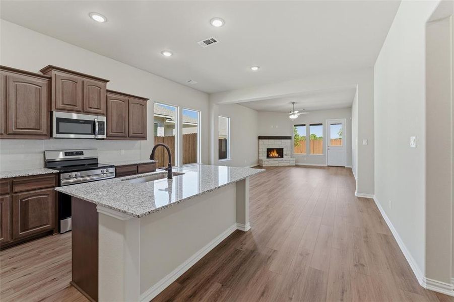 Kitchen featuring stainless steel appliances, a warm lit fireplace, light stone countertops, open floor plan, and recessed lighting