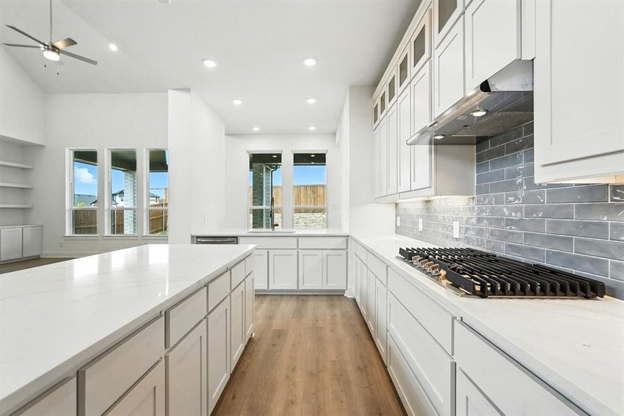 Kitchen featuring light stone counters, light wood-style floors, white cabinets, stainless steel gas stovetop, and under cabinet range hood Kitchen featuring light stone counters, light wood-style floors, white cabinets, stainless steel gas stovetop, and under cabinet range hood
