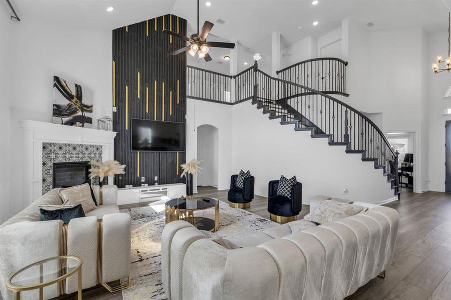 Living room featuring high vaulted ceiling, ceiling fan with notable chandelier, a tiled fireplace, and wood-type flooring