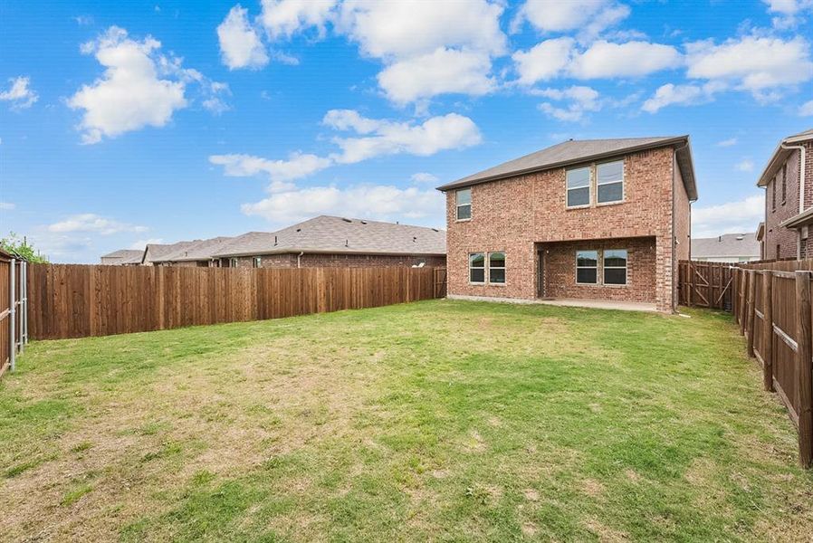 Expansive backyard featuring a privacy fence, a brick exterior two-story residence, and an integrated covered patio
