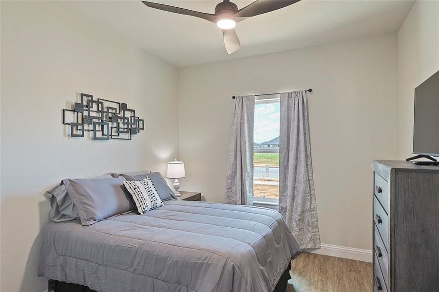 Bedroom featuring wood-finish flooring, a window with curtains, a ceiling fan with integrated lighting, and neutral-toned walls Bedroom featuring wood-finish flooring, a window with curtains, a ceiling fan with integrated lighting, and neutral-toned walls