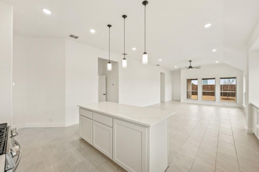 Open-concept kitchen with white island and pendant lights flowing into living area with tile floors
