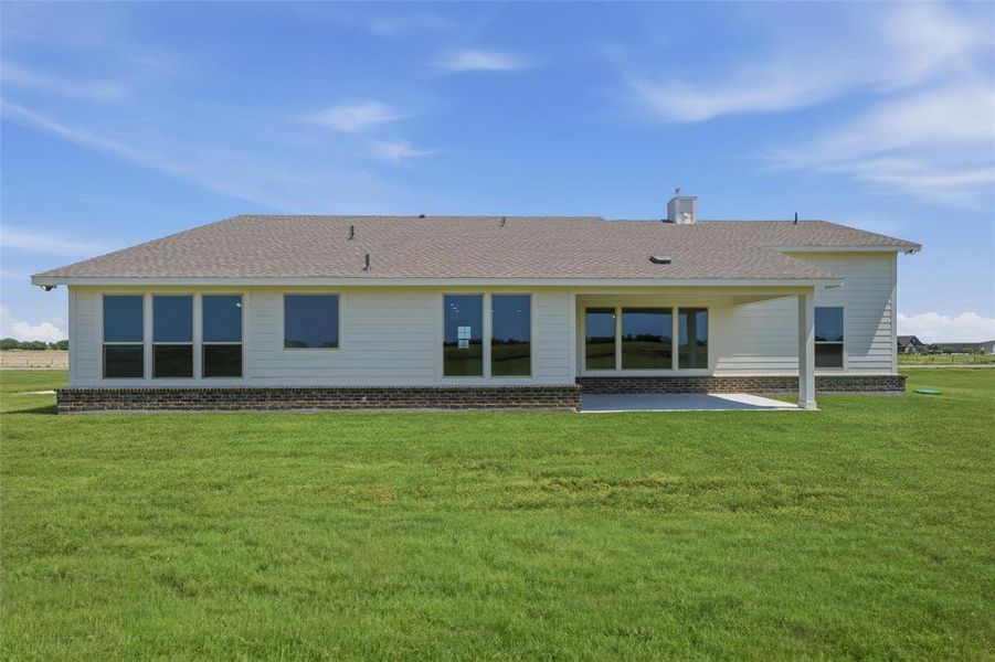 Expansive rear exterior featuring a covered patio, multiple large windows, a light-colored siding facade, and a stone-style foundation Expansive rear exterior featuring a covered patio, multiple large windows, a light-colored siding facade, and a stone-style foundation