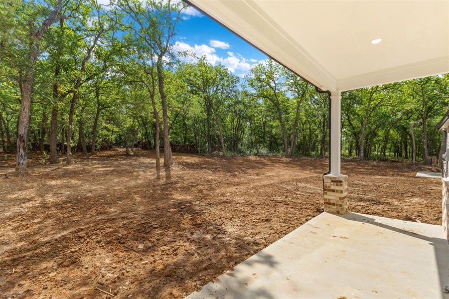 The property features an expansive backyard with mature trees and a covered patio with a brick column and recessed lighting