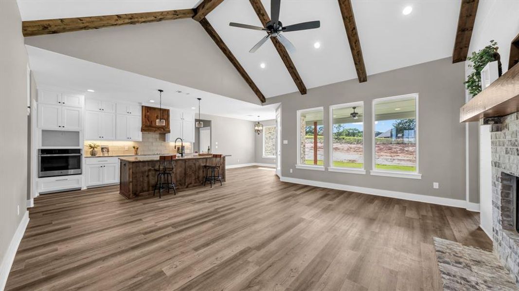 Large open concept living room featuring ceiling fan, beamed ceiling, high vaulted ceiling, a fireplace, and LVP floors