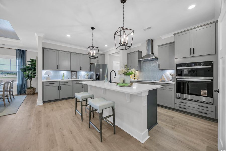 Kitchen with decorative backsplash, gray cabinets, a kitchen bar, decorative light fixtures, and light wood finished floors