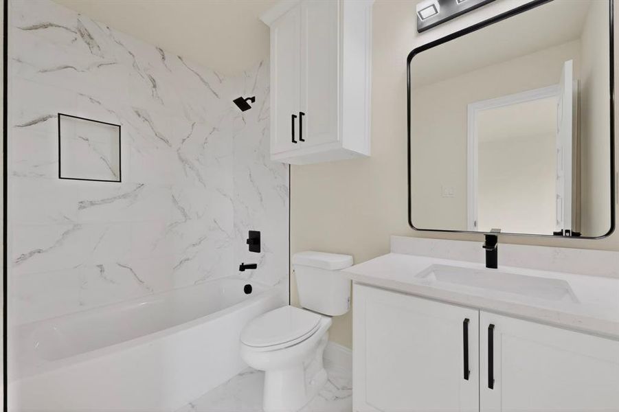 Full bathroom featuring a white tub with matte black fixtures, a built-in shower niche, and white marble-look wall tiling