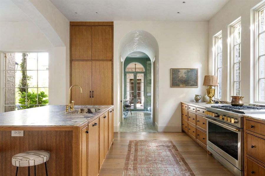 Kitchen featuring arched walkways, high end stainless steel range oven, brown cabinets, a kitchen island with sink, and light wood-style flooring