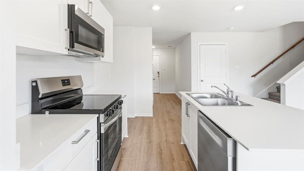 Kitchen featuring stainless steel appliances, light countertops, an island with sink, white cabinets, and light wood-type flooring