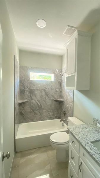 Full bathroom with tile flooring, toilet, vanity, and tiled shower / bath