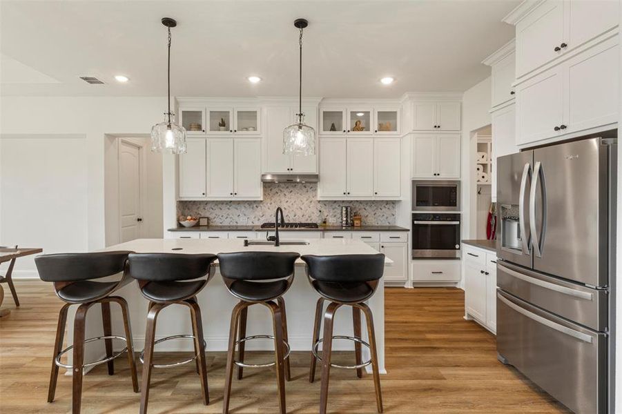 Kitchen with stainless steel appliances, tasteful backsplash, glass insert cabinets, white cabinets, and recessed lighting Kitchen with stainless steel appliances, tasteful backsplash, glass insert cabinets, white cabinets, and recessed lighting