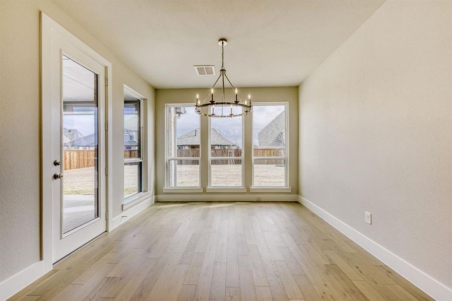 Unfurnished dining area featuring suspended lighting, light wood-style flooring, and a textured wall
