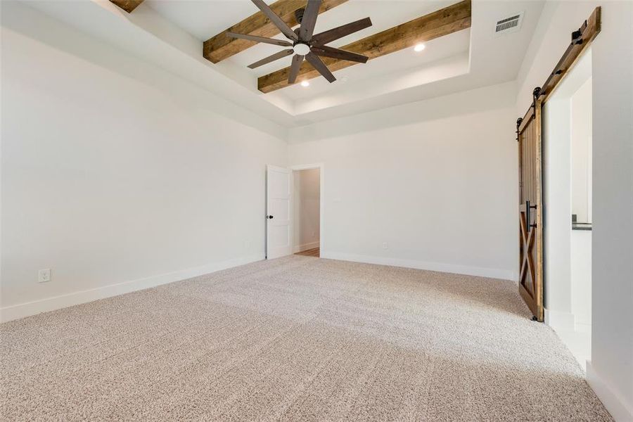 Carpeted spare room with a towering ceiling, a tray ceiling, ceiling fan, a barn door, and beamed ceiling