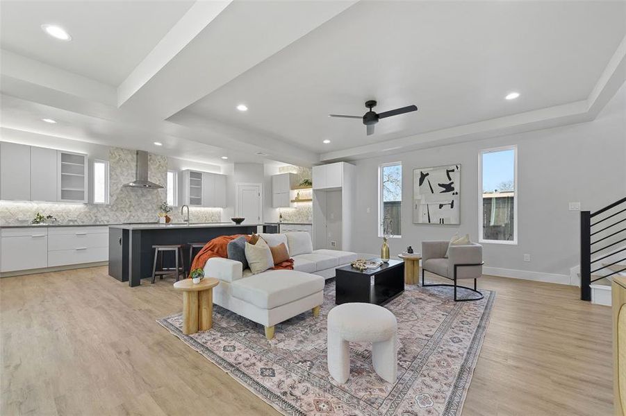 Living room with ceiling fan, sink, a tray ceiling, and light wood-type flooring