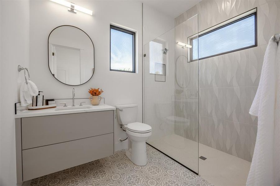 A stylish downstairs bathroom showcases a glass-enclosed shower, a sleek vanity, and decorative floor tiling.