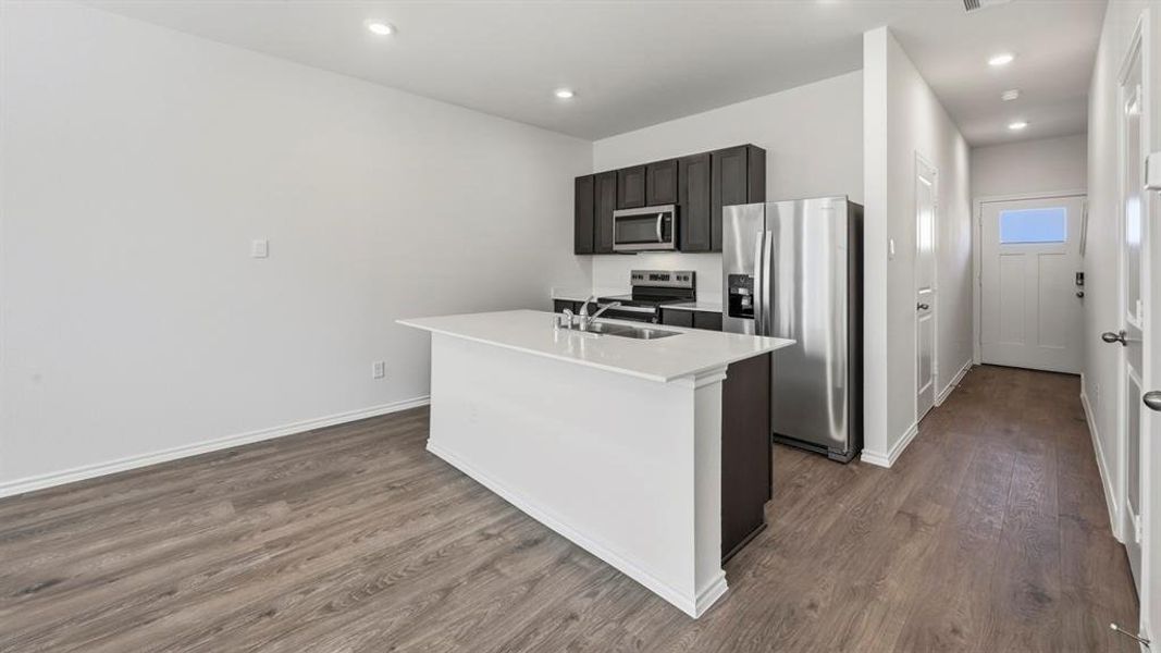 Kitchen featuring appliances with stainless steel finishes, a center island with sink, dark wood-type flooring, recessed lighting, and light stone countertops