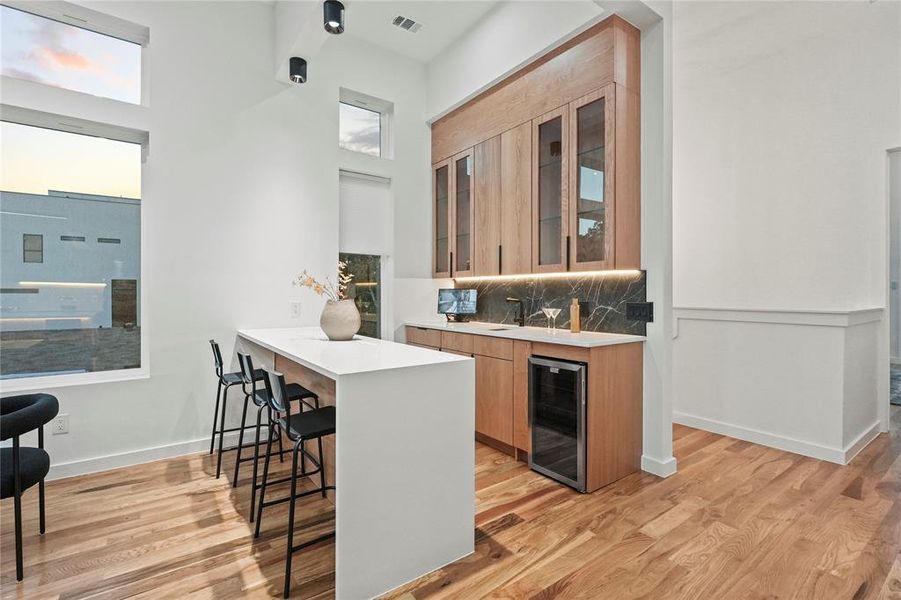 Kitchen featuring a kitchen bar, wine cooler, backsplash, and light hardwood / wood-style floors