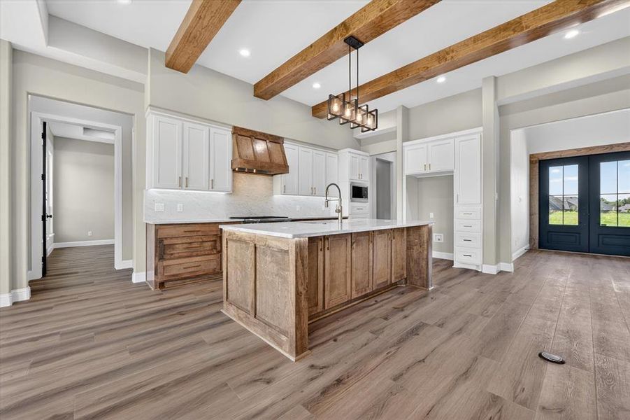 Kitchen featuring wood-finish flooring, exposed wood ceiling beams, a large island with white countertop, white upper cabinetry, and wood-finish lower cabinetry