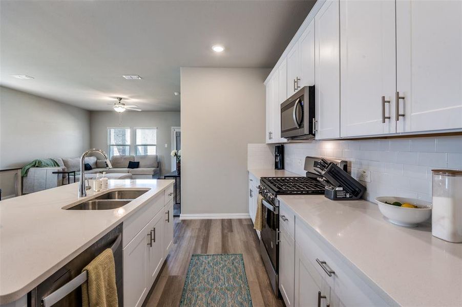 Kitchen featuring white cabinets, stainless steel appliances, open floor plan, light stone counters, and tasteful backsplash